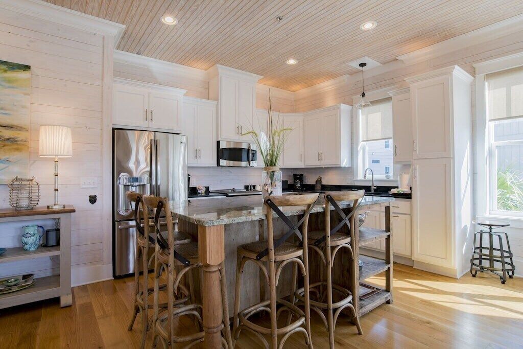 A modern kitchen with white cabinetry, a stainless steel refrigerator, a microwave, and a wooden island with bar stools.