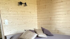 A bedroom with a wooden wall, a bed with a grey mattress and pillows, and a light switch. - Atypical gîte for 4 people 15 min from Angers (Saint-Martin-du-Fouilloux)