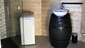 A bathroom with wooden walls, a glass shower enclosure, a white sink on a black barrel, and a round mirror above the sink. - Atypical gîte for 4 people 15 min from Angers (Saint-Martin-du-Fouilloux)