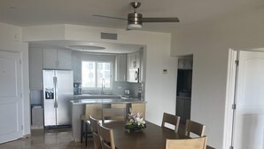 Un comedor amplio con una mesa y sillas de madera, una cocina al fondo y un ventilador de techo.