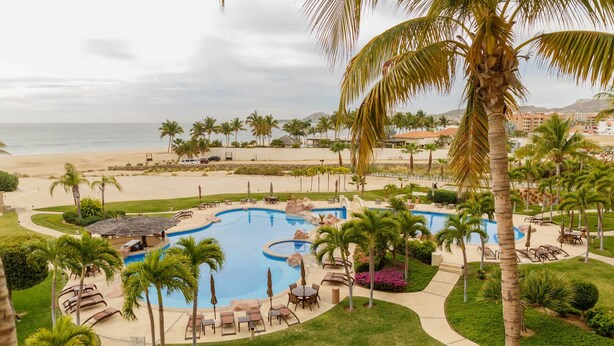 Un resort con una piscina grande rodeada de palmeras, sillas de descanso y vistas a la playa.