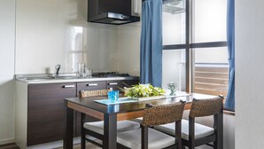 Een kleine keuken met een eethoek, met een tafel en stoelen, een raam met gordijnen en uitzicht op het exterieur.