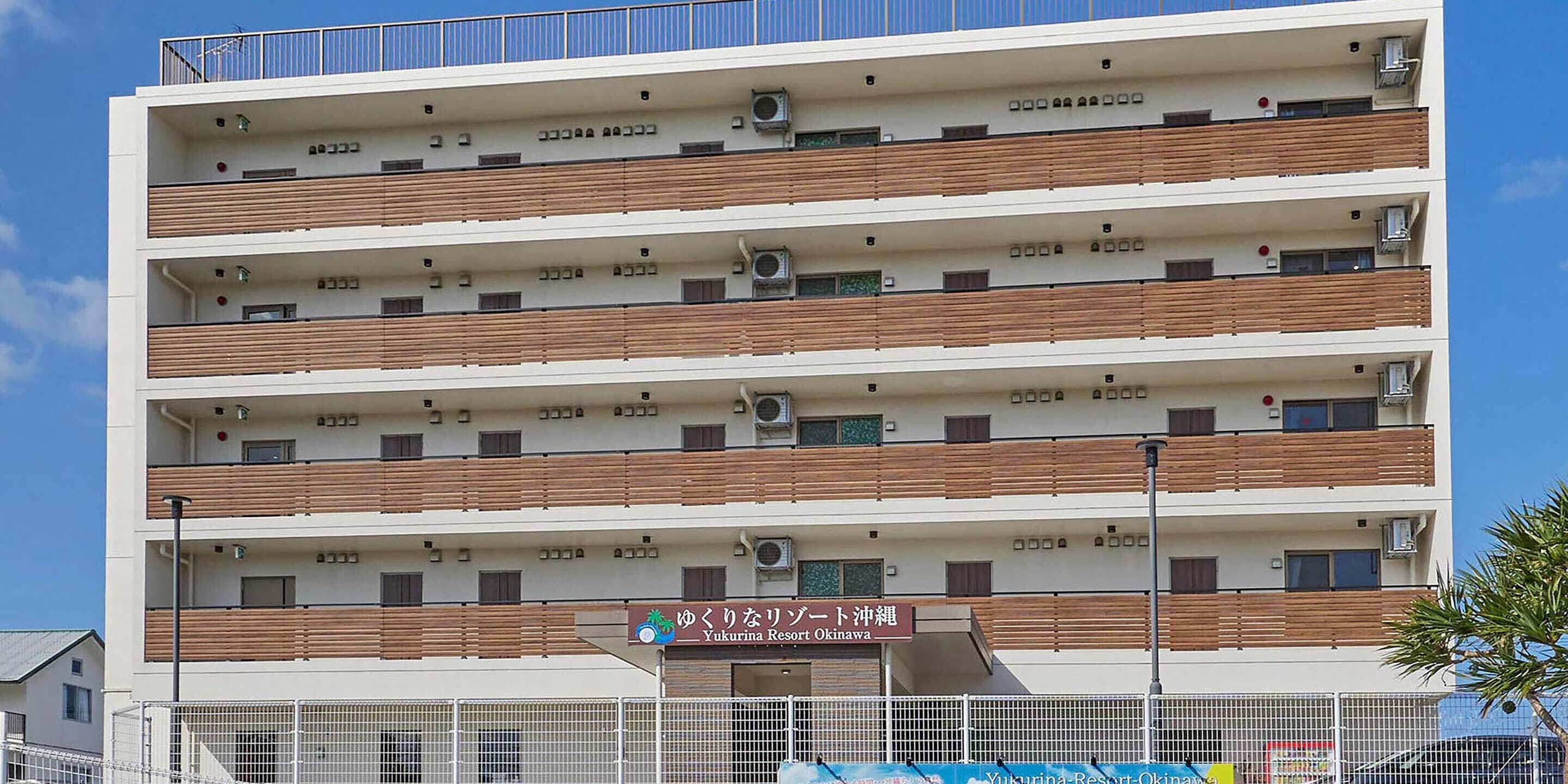 A multi-story hotel with balconies, air conditioning units, and a sign indicating it is the Yukurina Resort Okinawa.