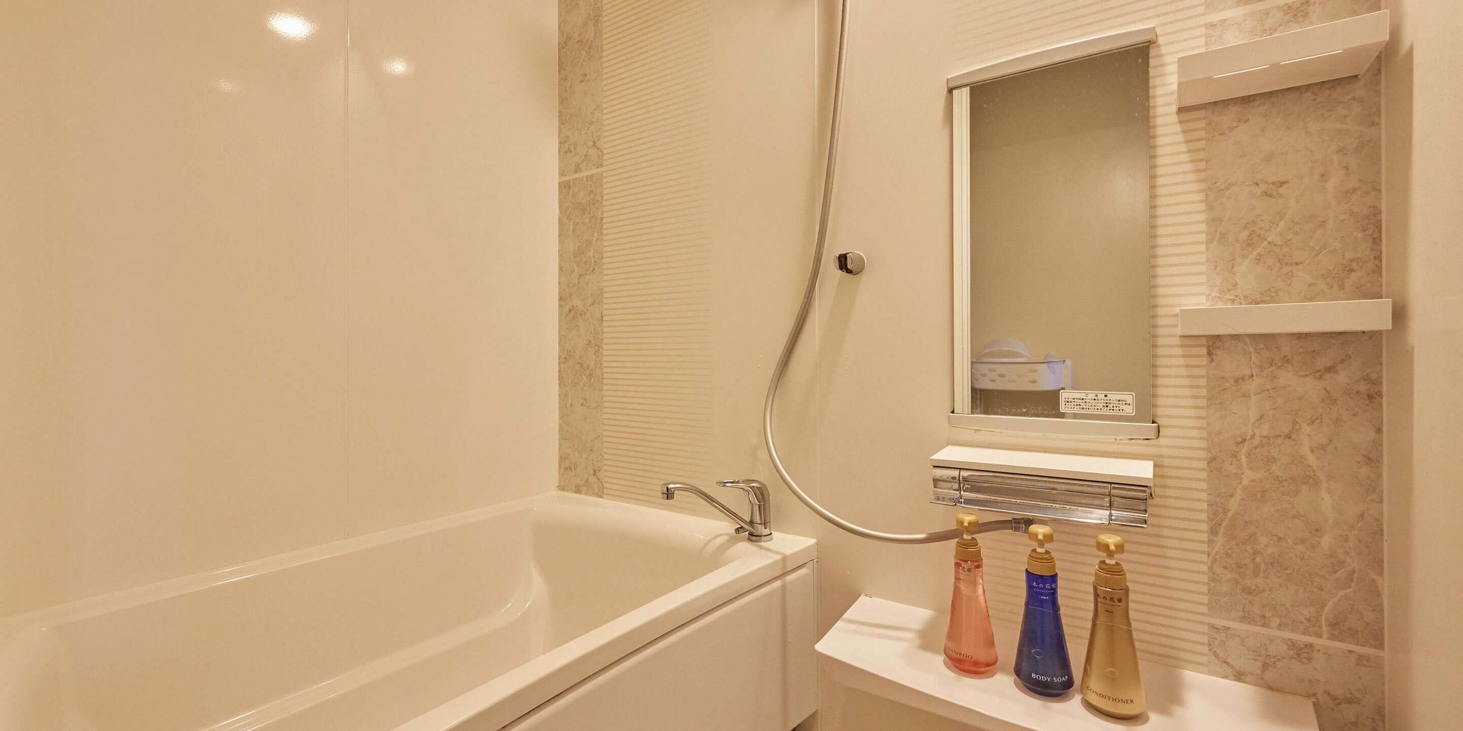 Uma casa de banho com banheira, espelho e uma prateleira com três frascos de shampoo e condicionador.