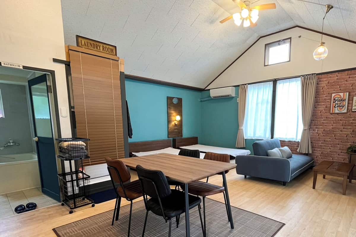 A room with a dining table, chairs, a sofa, a small bed, a laundry room sign, and a brick wall.