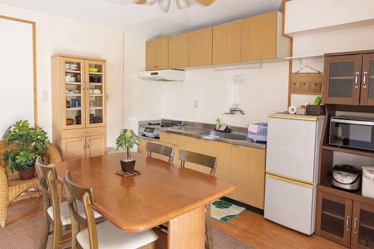 A compact kitchen with wooden cabinets, a microwave, a refrigerator, and a dining table with chairs.