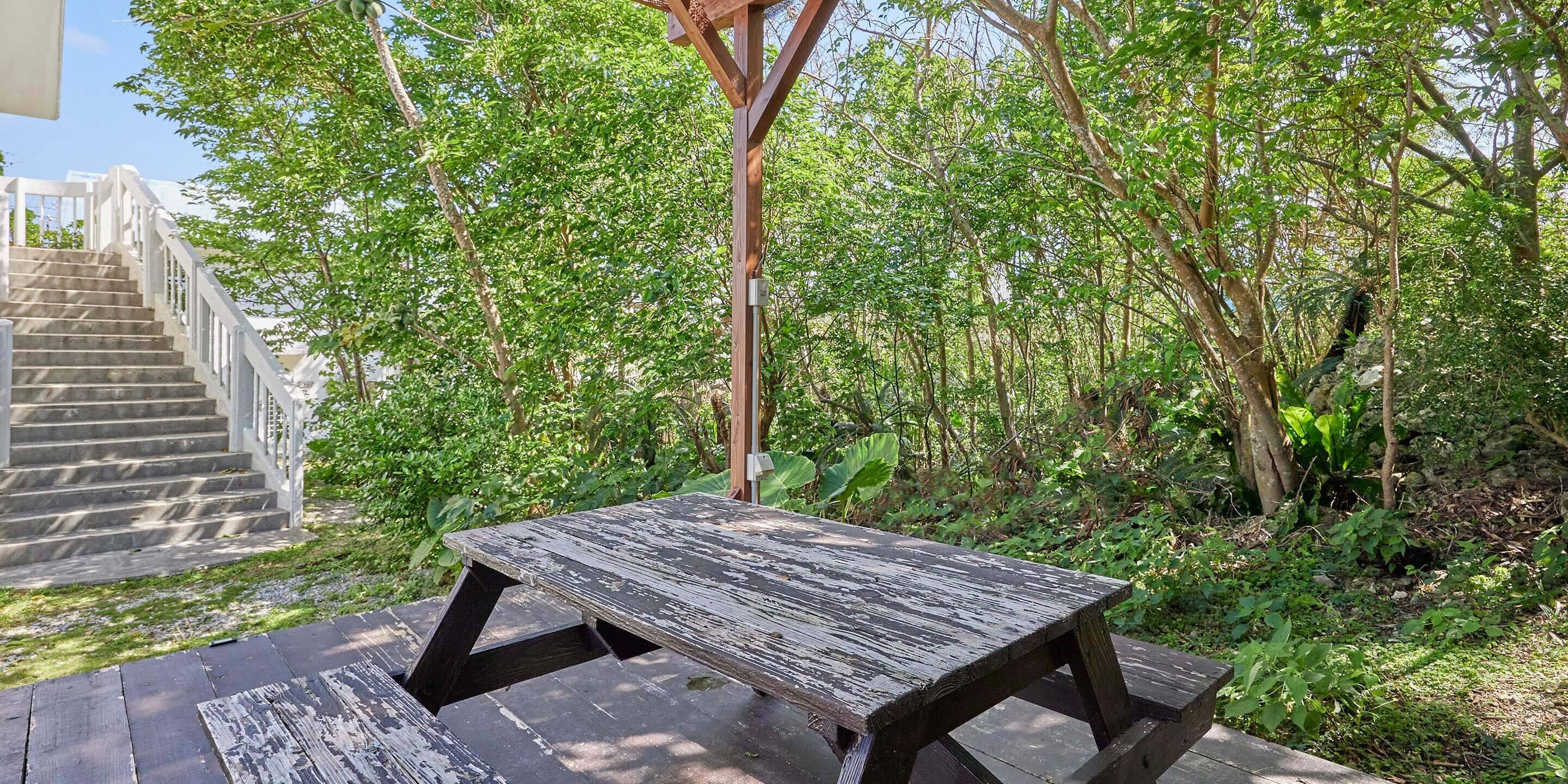 A wooden picnic table in a garden with a staircase and dense foliage in the background.