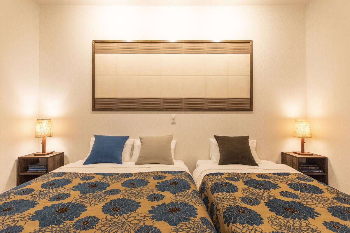 A hotel room with two beds, each with a floral-patterned bedspread, a large mirror above, and bedside lamps.