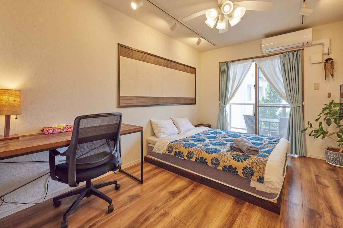 A hotel room with a bed, desk, chair, and a ceiling fan.