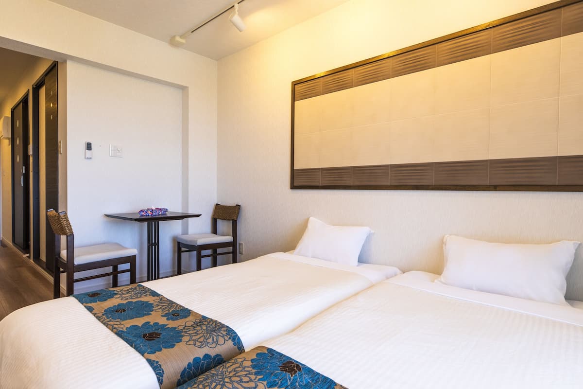 A hotel room with two beds, a small table, and a chair.