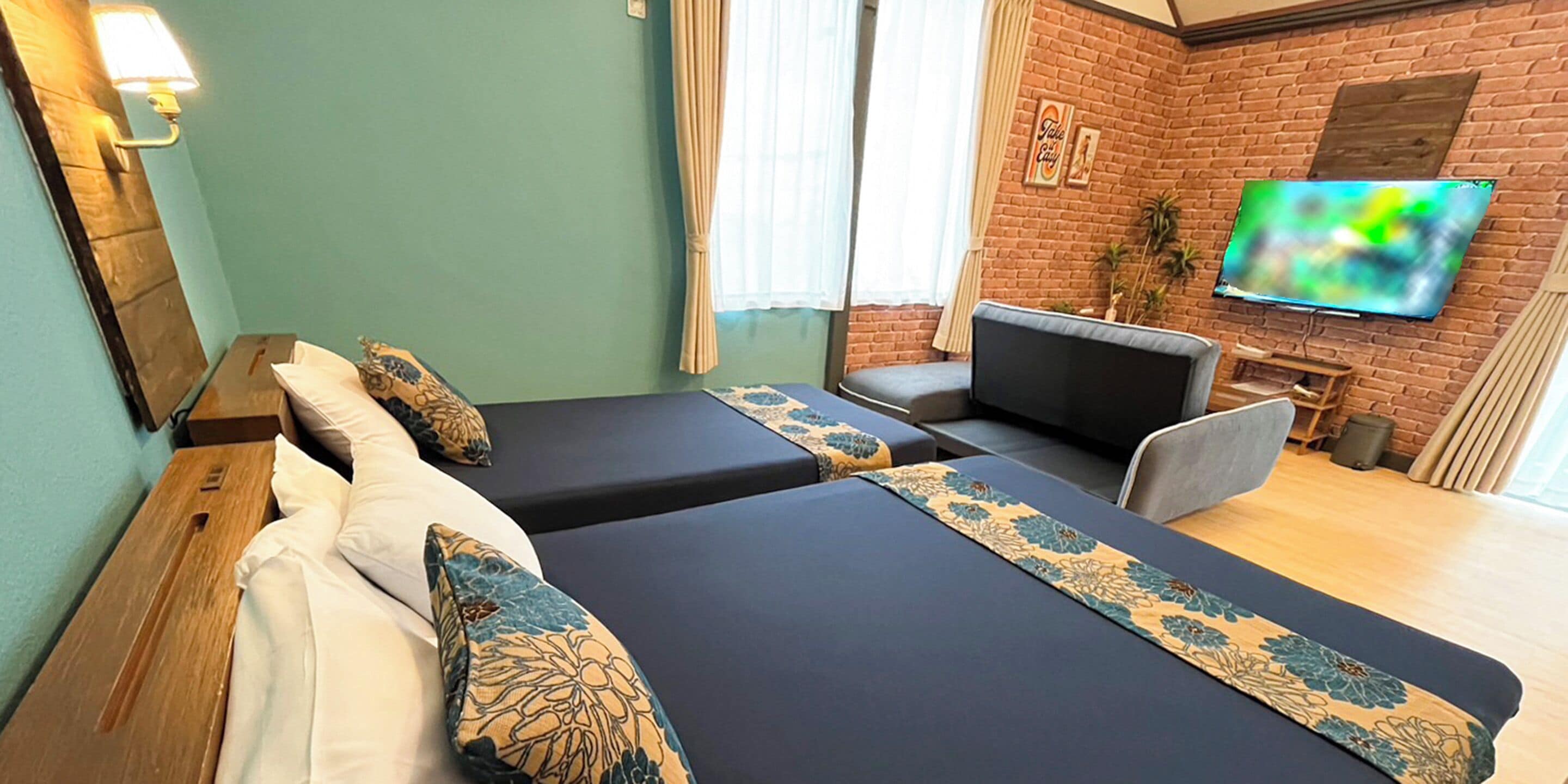 A hotel room with two single beds, a sofa, a TV, and a brick wall.
