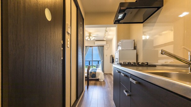 Een smalle gang die leidt naar een slaapkamer met uitzicht, een kitchenette met moderne apparatuur, en een donker houten deur.