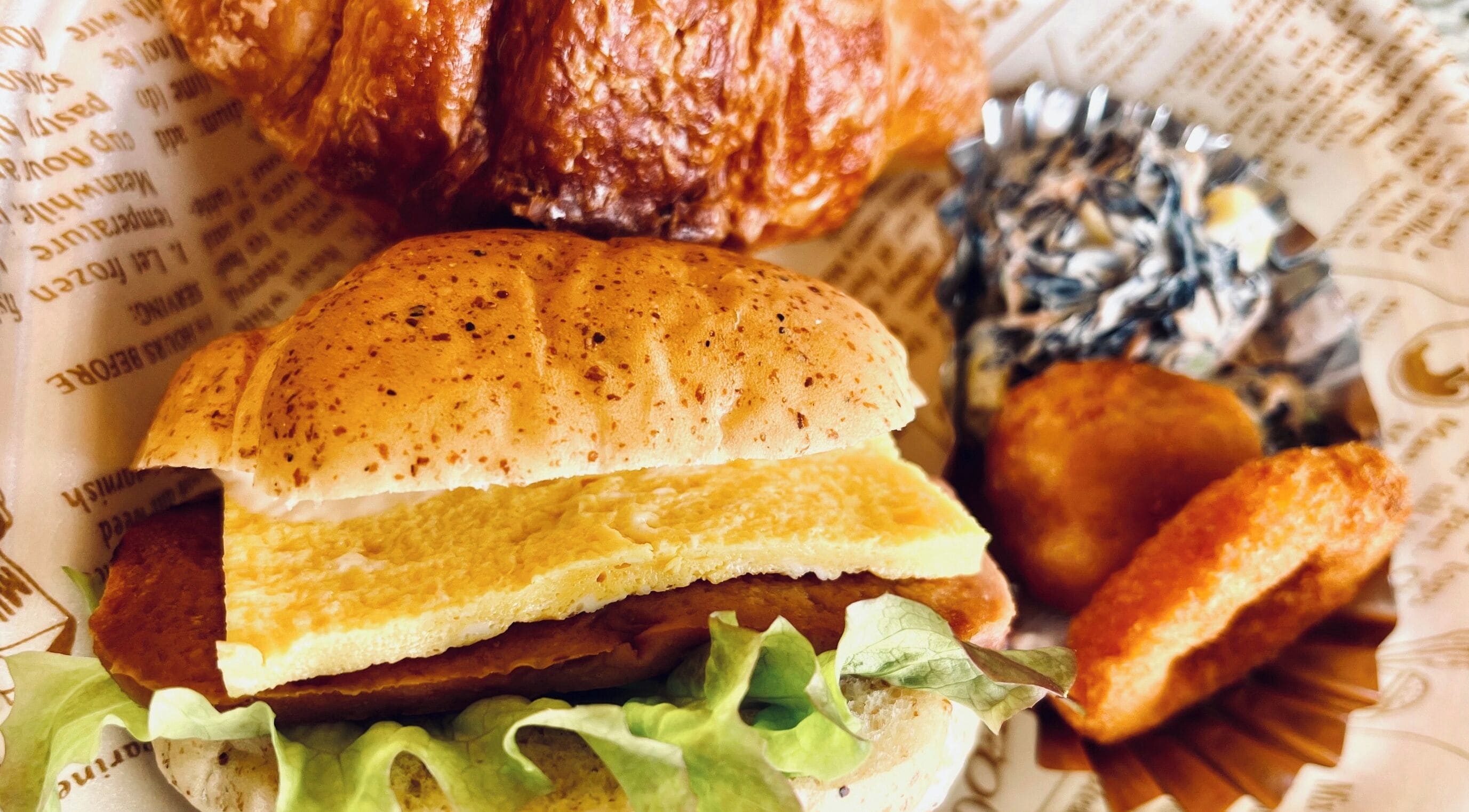A sandwich with lettuce and a bun, a fried item, and a small round fried item on a paper with text.