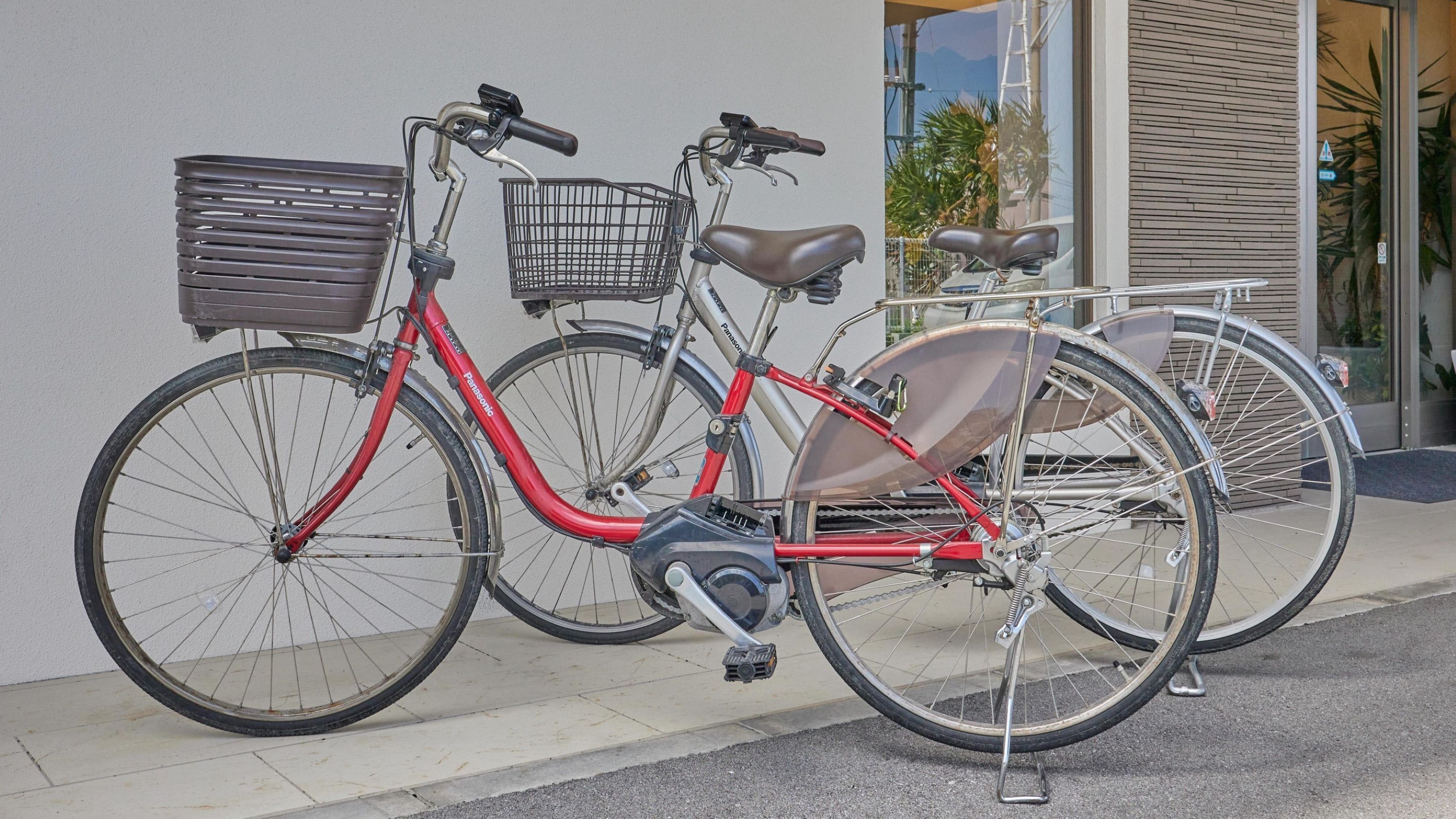 A red bicycle with a basket and a seat attached, parked against a building.