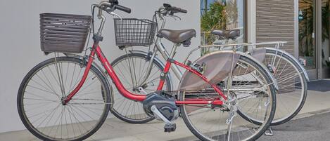 A red bicycle with a basket and a seat attached, parked against a building.