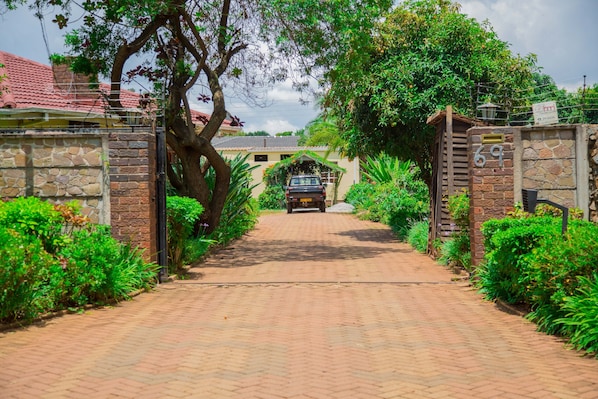 Pathway leads to a gated entrance surrounded by lush greenery and a stone wall.