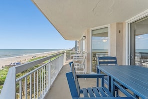 Un balcon avec vue sur la plage, une table, des chaises et une porte vitrée.