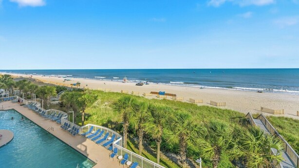 A beach resort with a swimming pool, lounge chairs, and a lifeguard tower. - Cozy Corner Unit, Jacuzzi Tub and Recliner, Lazy River | Crescent Shores - S 312 (North Myrtle Beach)