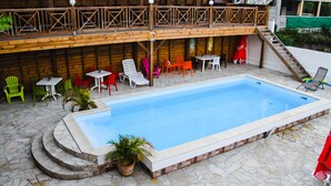 Ein Schwimmbecken mit einer Steindeck, umgeben von bunten Stühlen und Tischen.