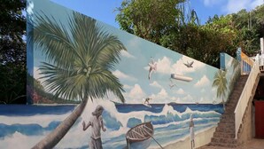 Ein Wandgemälde zeigt eine Strandansicht mit Palmen, einem Boot und Menschen.