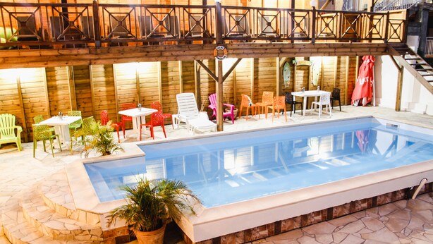Ein Hallenbad mit Steinböden, umgeben von verschiedenen Stühlen und Tischen.