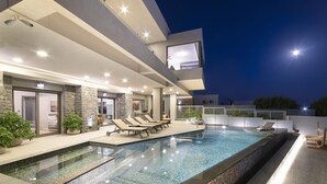 An outdoor swimming pool with lounge chairs, a stone wall, and a modern architectural design. - Beachfront Moonlight villa for large groups (Koutsouras)