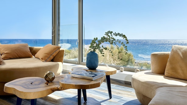 A modern living room with a large window overlooking the sea, featuring a sofa, coffee table, and decorative items. - Beachfront Moonlight villa for large groups (Koutsouras)