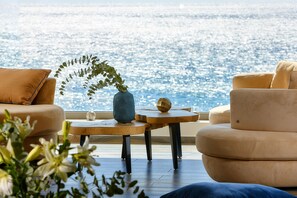 Una sala de estar moderna con vista al mar, que incluye un sofá, una mesa de centro y un florero con una planta.