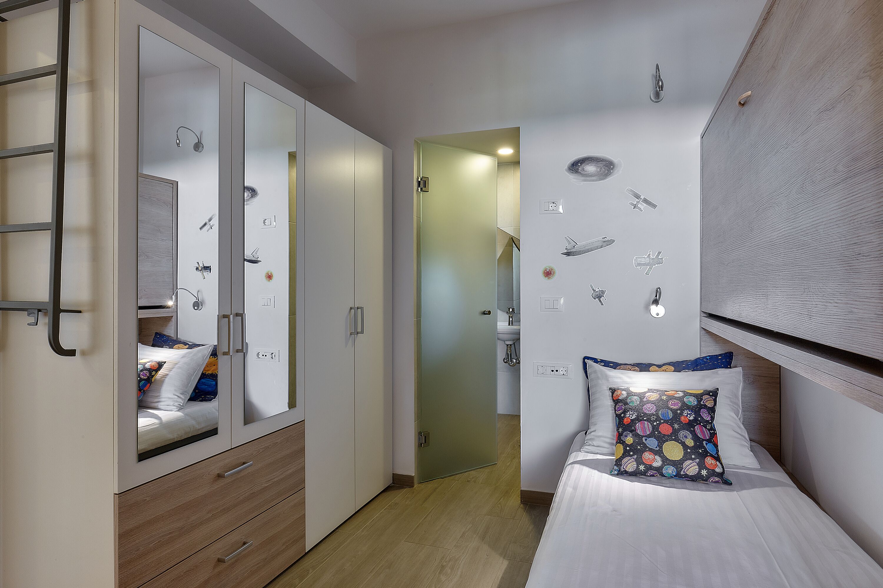 Een slaapkamer met een stapelbed, een garderobe met spiegeldeuren, een nachtkastje en een muur versierd met vliegtuigstickers.