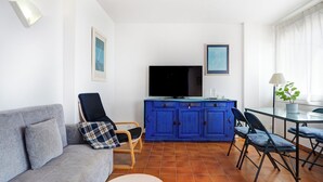 Un salon comprenant un canapé, un buffet bleu, un téléviseur et un coin repas avec des chaises et une table.