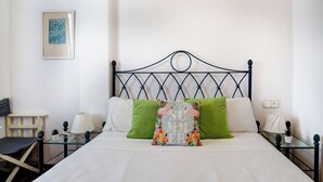Un lit bien fait, avec du linge de lit blanc, une tête de lit en métal noir et deux coussins verts.