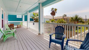 A covered porch with wooden flooring, green and blue Adirondack chairs, and a white railing. - Private Heated Pool, Golf Cart for Entire Stay, Game Room, Pet Friendly (Port Aransas)