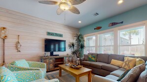 A living room with a television, wooden panel walls, a ceiling fan, and a sign that reads "Beach Therapy". - Private Heated Pool, Golf Cart for Entire Stay, Game Room, Pet Friendly (Port Aransas)