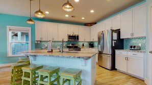 A kitchen with white cabinets, a central island with stools, stainless steel appliances, and pendant lighting. - Private Heated Pool, Golf Cart for Entire Stay, Game Room, Pet Friendly (Port Aransas)