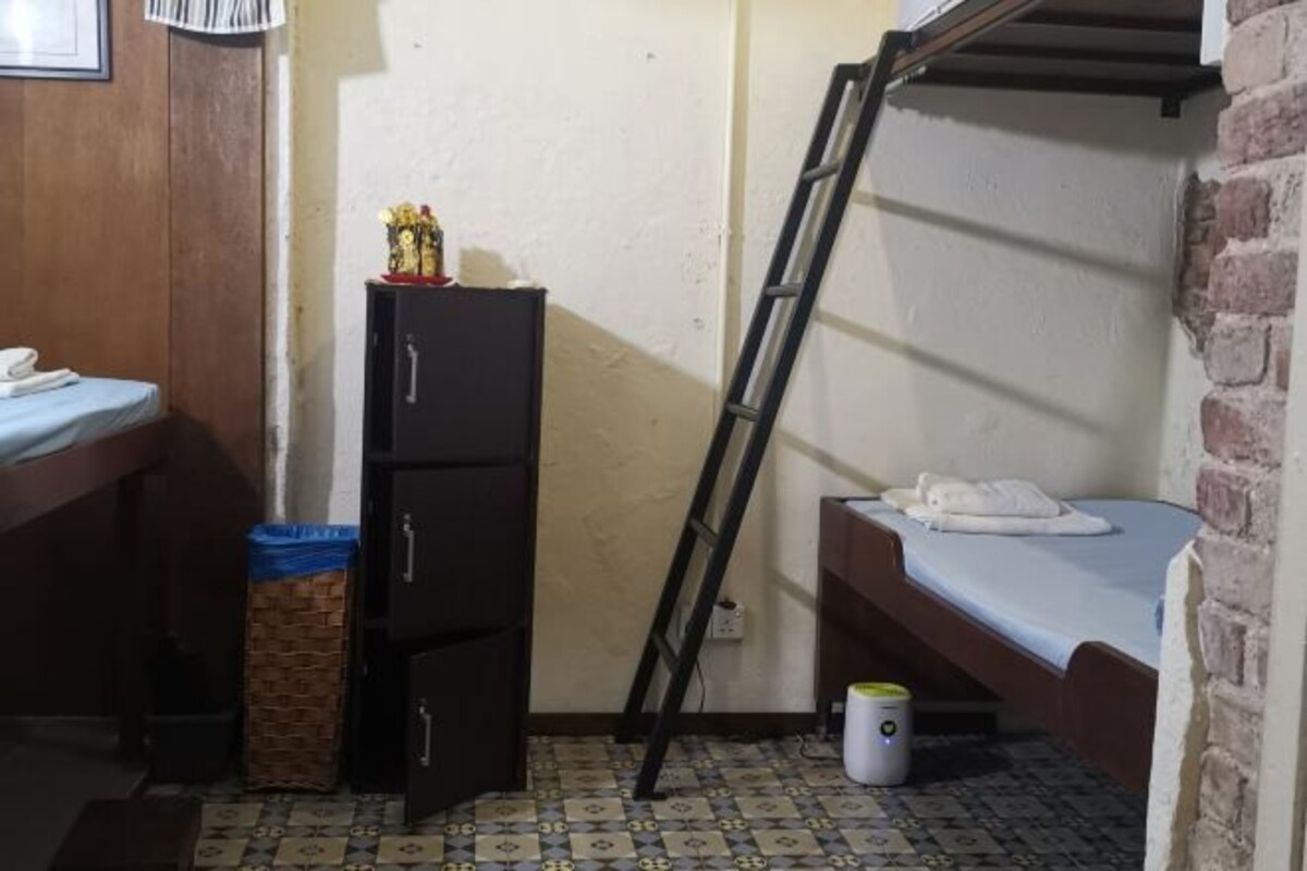 Una habitación pequeña y funcional con una cama litera, un armario, un bote de basura y una escalera.