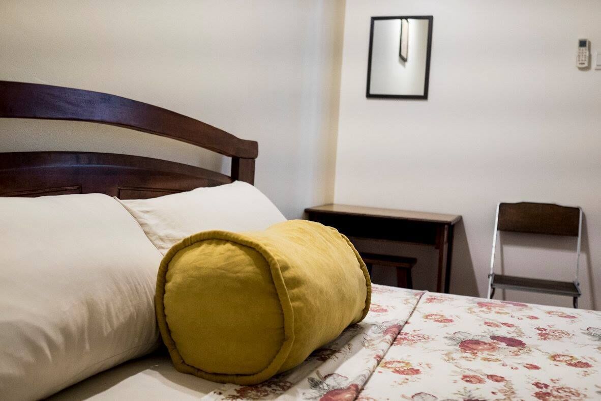 Una cama bien hecha con cabecera de madera, almohada amarilla y colcha estampada con motivos florales.