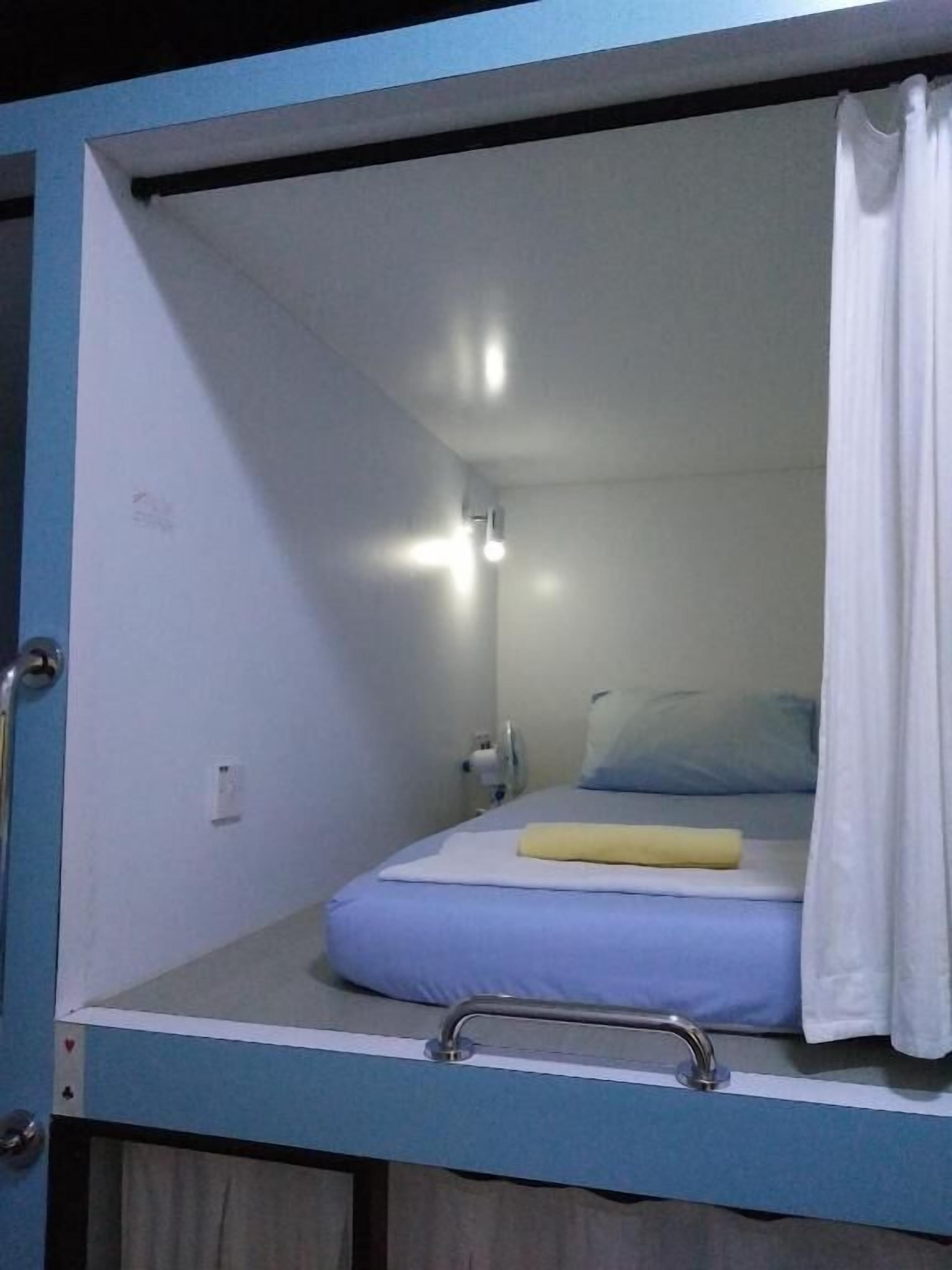 A bunk bed with a blue headboard, a white curtain, and a bedside table with a lamp.