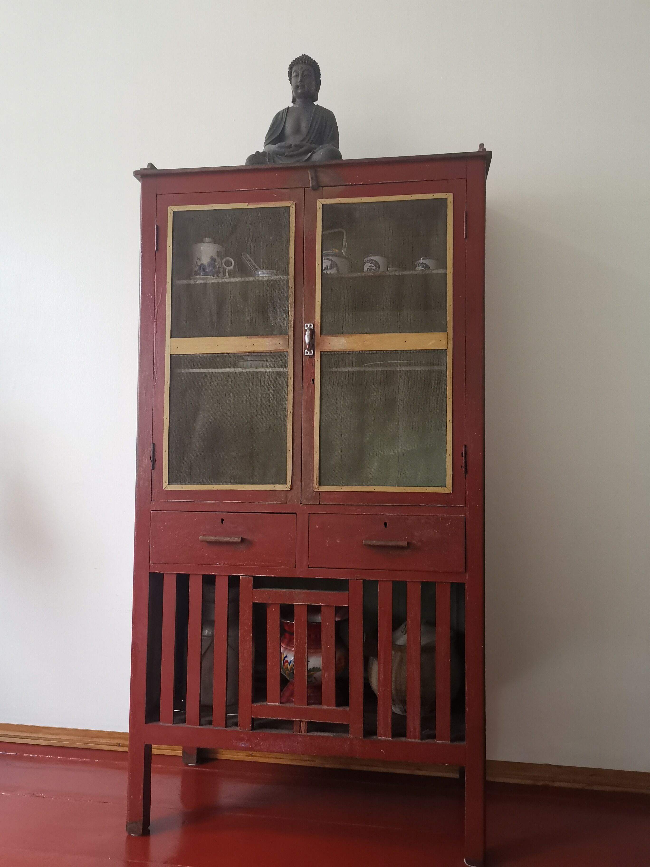 Un meuble rouge avec des portes en verre et une statue sur le dessus.