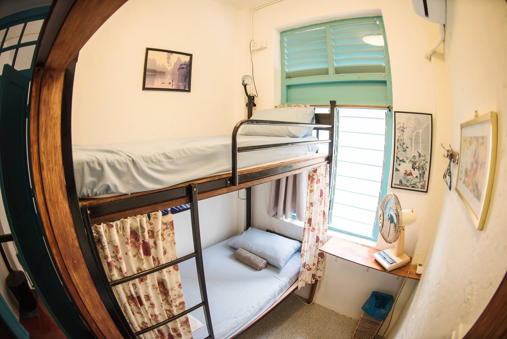 A bunk bed room with a window, a fan, and a small desk.