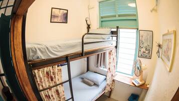 A bunk bed room with a window, a fan, and a small desk.