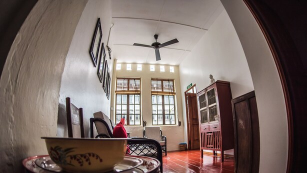 Una habitación con comedor que incluye una mesa con platos apilados y un tazón, un ventilador de techo y una vista a través de un arco hacia otra habitación con un armario y una puerta.