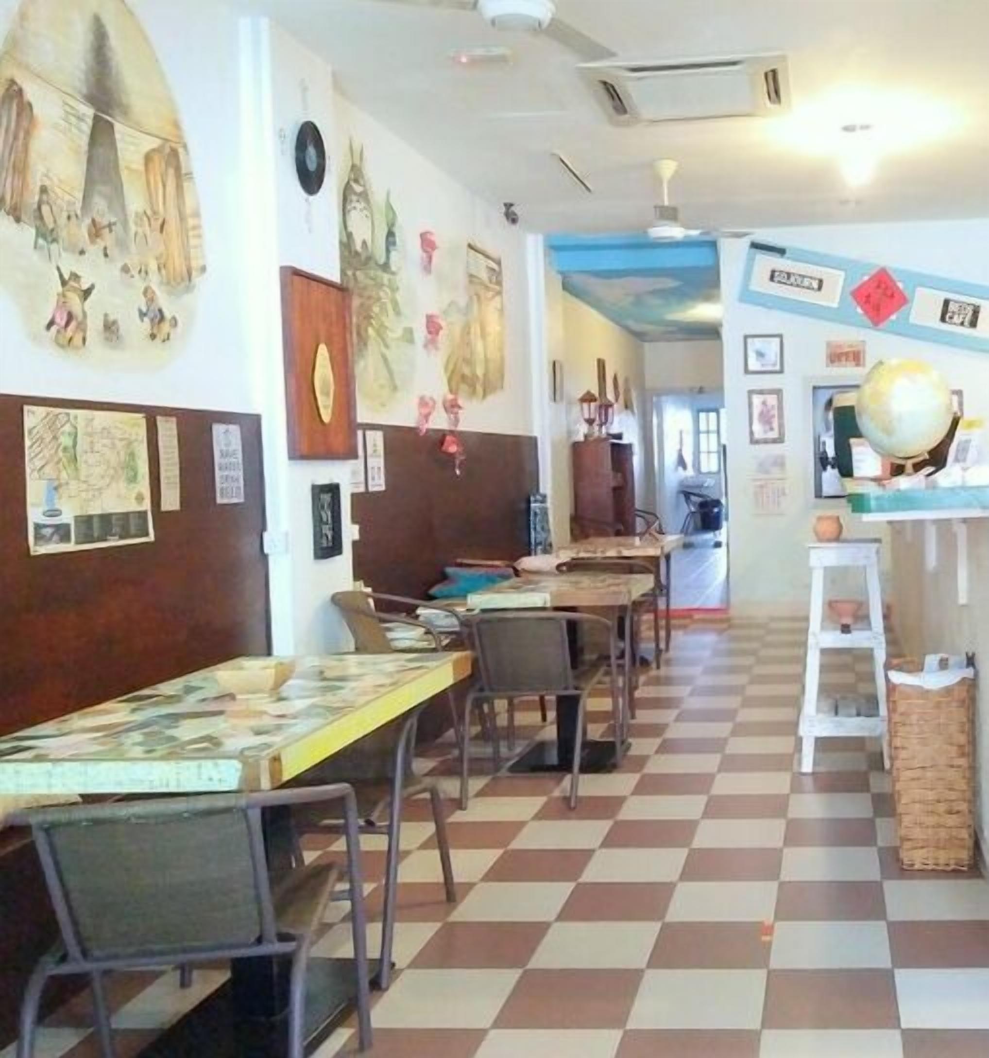 Ein Restaurant mit Schachbrettböden, mehreren Tischen, Stühlen und verschiedenen Wanddekorationen, darunter Kunstwerke und ein Globus.
