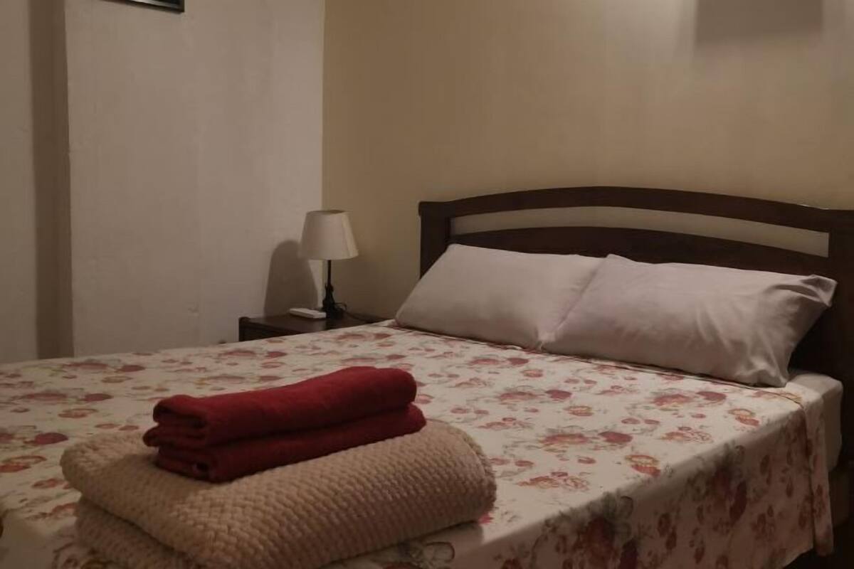 A bed with a floral bedspread, two pillows, a nightstand with a lamp, and folded towels.