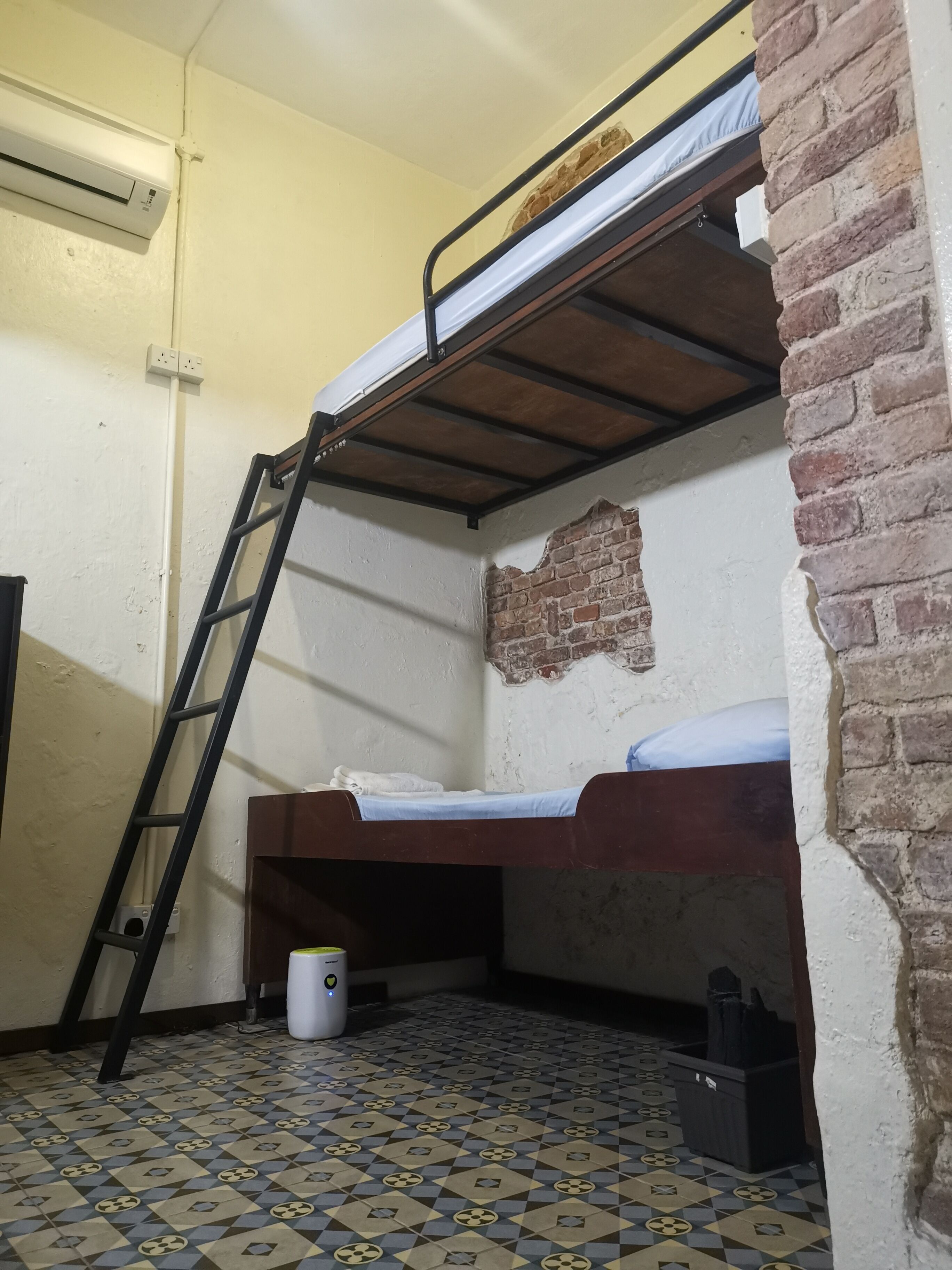 A bunk bed room with a ladder, a brick wall, and a patterned floor.
