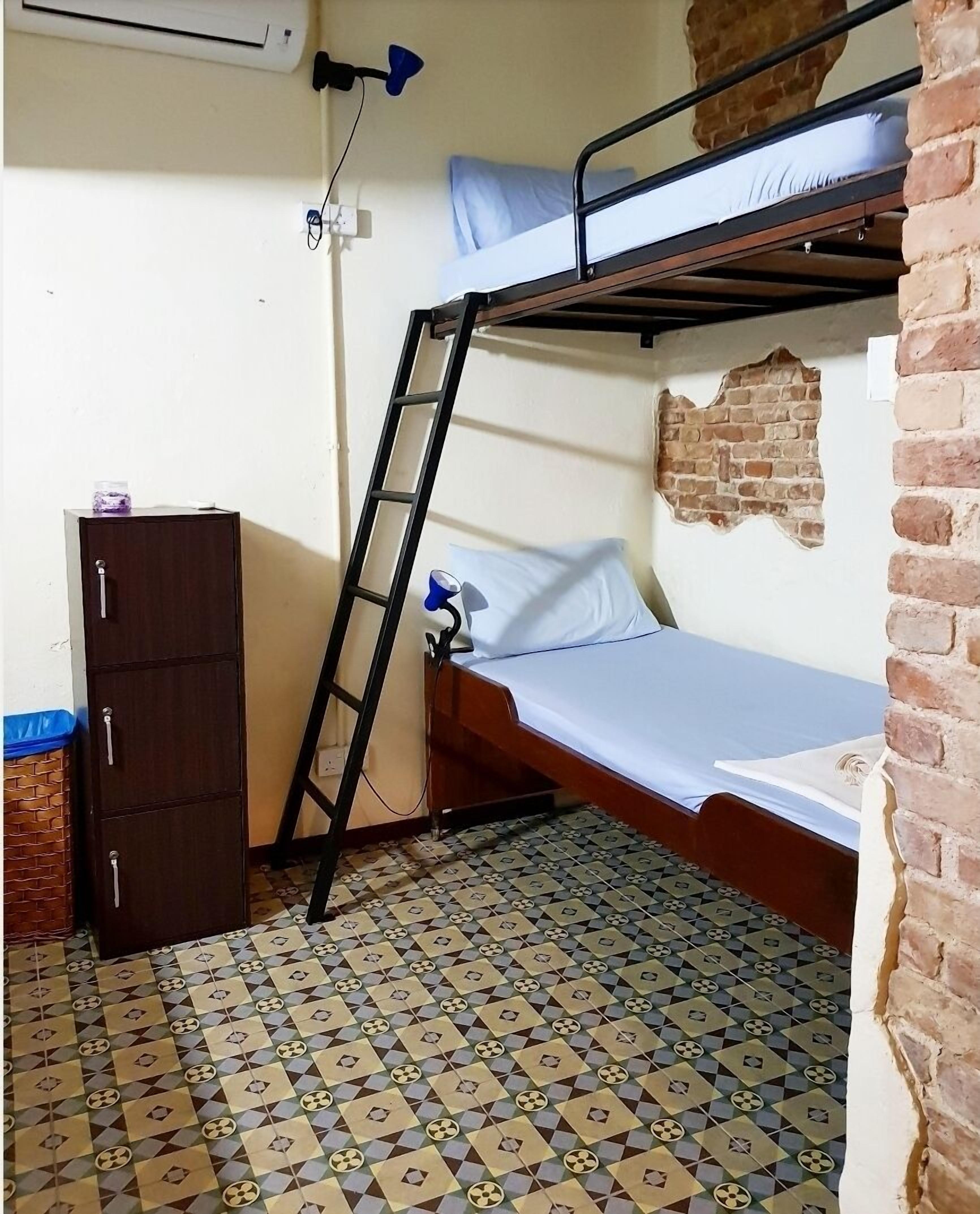 Une petite pièce compacte comprenant un lit superposé, un bureau avec une chaise, une armoire et un sol à motifs.