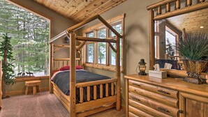Camera da letto in legno in stile baita, con un letto a baldacchino, una cassettiera in legno e ampie finestre che offrono vista sugli alberi.