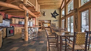 Un interno rustico con camino in pietra, zona pranzo in legno e ampie finestre che si affacciano su un paesaggio innevato.