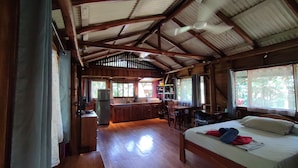 Een rustieke hut met houten inrichting, een bed met kussens, een eettafel en een keukenhoek.
