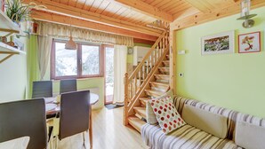 L’intérieur chaleureux d’un chalet comprend un coin repas, un escalier en bois et un salon avec un canapé et des coussins.
