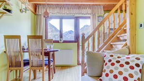 Une pièce chaleureuse avec un escalier en bois, un coin repas avec des chaises et une table, et une fenêtre donnant sur la montagne.